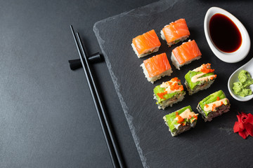 Set of tasty sushi rolls with salmon, avocado and tobiko caviar on black slate board.