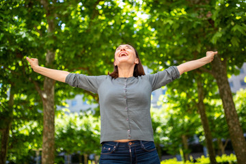 carefree older woman smiling with arms outstretched in nature park