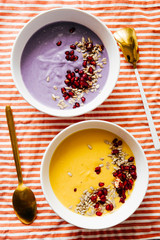 Pumpkin and coconut soup with pumpkin seeds and pomegranate and the other violet potatoes soup, on a colored striped towel,flat lay composition, healthy warm food for autumnal and winter season.