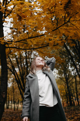 Fototapeta na wymiar Autumn portrait of a young girl in an autumn park in a gray coat. Posing at a photo shoot in nature.