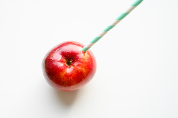 a ripe juicy bright red apple and in it a striped white and green paper drinking straw, located on a white background. space for text