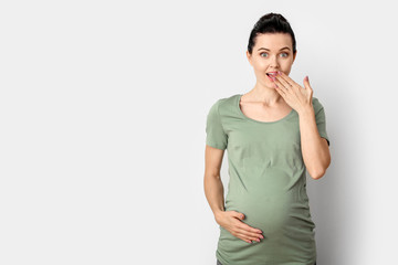 Beautiful surprised pregnant woman on light background
