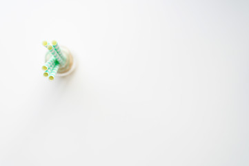 blurred pile of paper striped white and green drinking straws for party in clear glass small bottle on white background. space for text