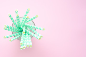 pile of paper striped white and green drinking straws for party in clear glass cup on pink background