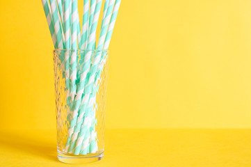 pile of paper striped white and green drinking straws for party in clear glass cup on yellow background. space for text