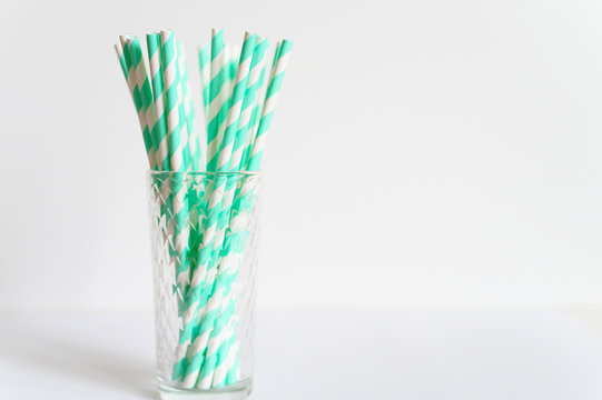 Pile Of Paper Striped White And Green Drinking Straws For Party In Clear Glass Cup On White Background. Space For Text