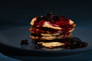 Sweet pancakes with blackcurrant jam on top in a plate on the table.