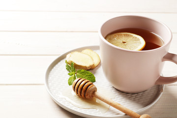 cup of hot tea with ginger, lemon and mint on a white wooden background