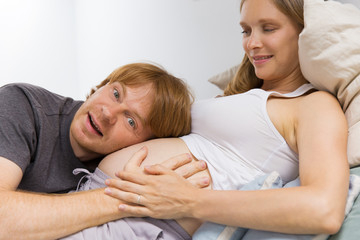 Excited expectant couple having fun at home. Happy future father listening to baby bump. Future parents concept