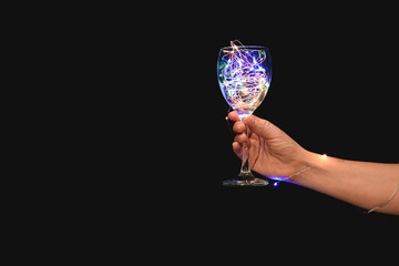 Female hand with beautiful glowing garland in glass on dark background