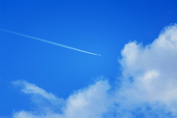 Plane with white footprint in the blue sky with clouds_