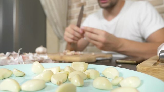 a man peels garlic sitting at a table on a background of a brick wall.