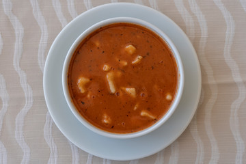 Red tomato soup with dumplings in a white bowl, close up