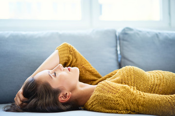 Cheerful young woman lying on sofa with eyes closed and relaxing