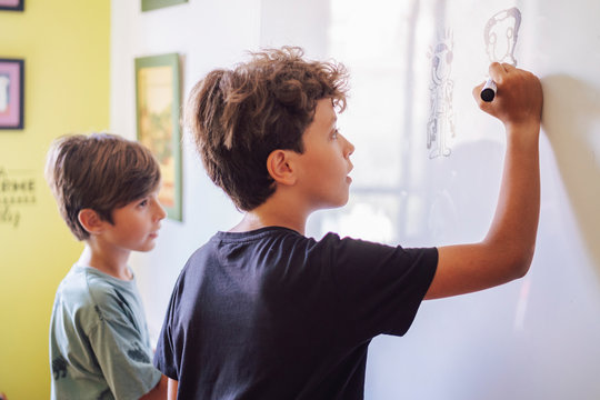 Focused boy with a friend drawing on a whiteboard