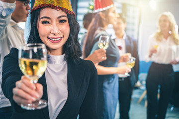Business social gathering party,New Year's Eve celebration. Happy Asian businesswoman in party holding wine glass with her colleagues in the background.