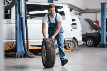 White and black colored cars behind. Employee in the blue colored uniform works in the automobile salon