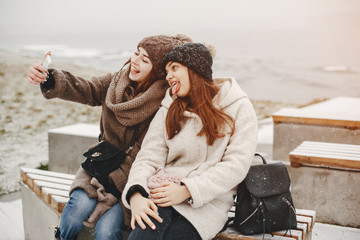 Fototapeta premium two bright and merry girls sitting in the frozen snowy park and use the phone