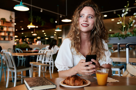 Smiling young woman with smartphone in a cafe having breakfast