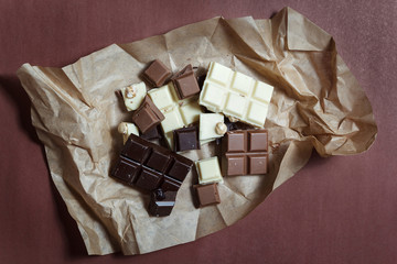 White, dark and milk chocolate on paper on brown background.