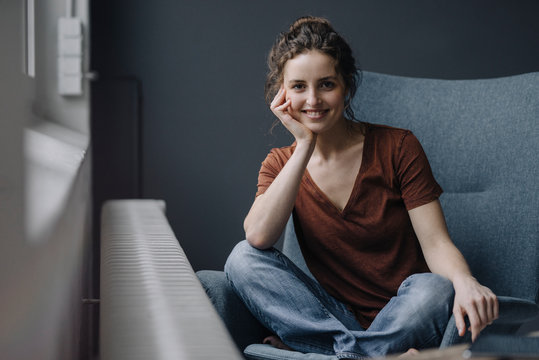 Portrait of smiling young woman sitting on lounge chair at home