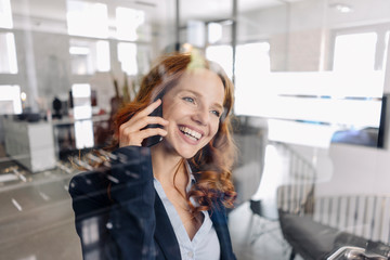 Happy redheaded businesswoman on the phone in office