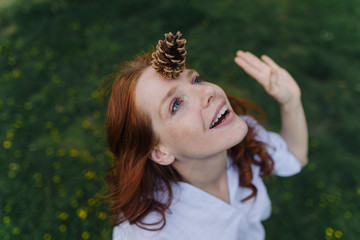 Redheaded woman balancing a pine cone on her forehead