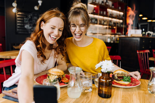 Two happy female, friends having burger and taking a selfie in a restaurant