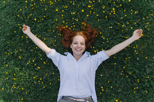 Portrait of happy redheaded woman lying on a flower meadow