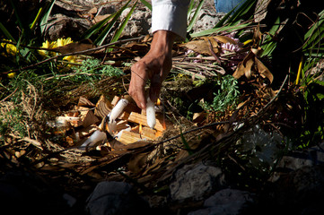 A mayan priest is lighting ceremonial fire with candles in a stone fire pit.