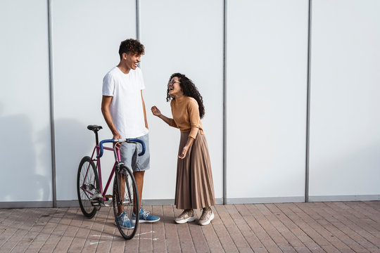 Happy couple with bicycle standing in front of white fence, laughing