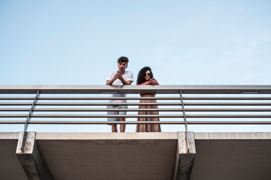 Young couple standing on bridge, using smartphones