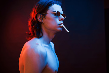 Fototapeta premium Smoking cigarette. Studio shot in dark studio with neon light. Portrait of serious man