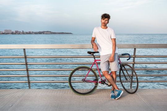 Young man with bicycle, standing on bridge by the sea