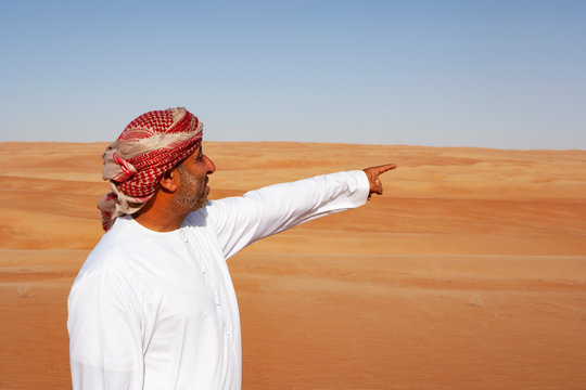 Bedouin in National dress standing in the desert, pointing at distance, Wahiba Sands, Oman