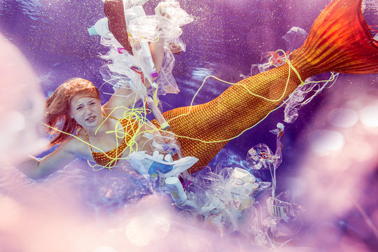 Teenage mermaid girl surrounded by plastic waste under water