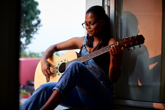 Woman playing guitar sitting at the edge of the window