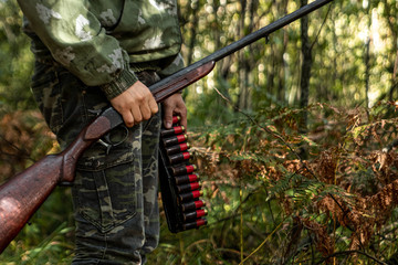 A hunter with a gun in his hands in hunting clothes in the autumn forest close-up. The hunting...