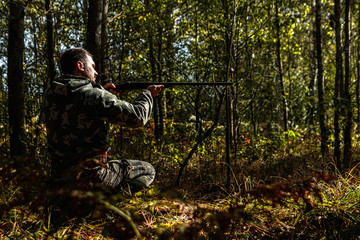 Hunter man in camouflage with a gun during the hunt in search of wild birds or game on the background of the autumn forest. Autumn hunting season. The concept of a hobby, killing.