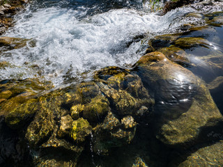Fototapeta na wymiar stream of river water with stones below and white foam waterfall