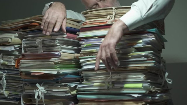 Exhausted businessman leaning on piles of paperwork