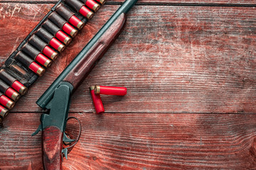 Shotgun and cartridges in patronage are lying on a wooden table top view. The hunting period, the...