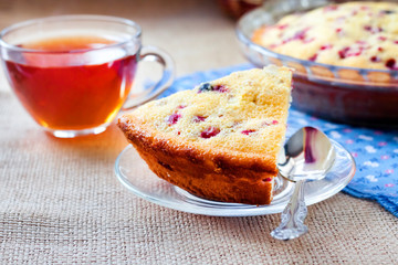 Piece of cowberry pie on glass plate and cup of tea