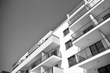  Fragment of a facade of a building with windows and balconies. Modern home with many flats. Black and white.