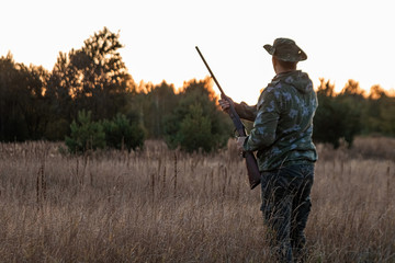 Silhouette of a hunter in a cowboy hat with a gun in his hands on a background of a beautiful sunset. The hunting period, the fall season is open, the search for prey.