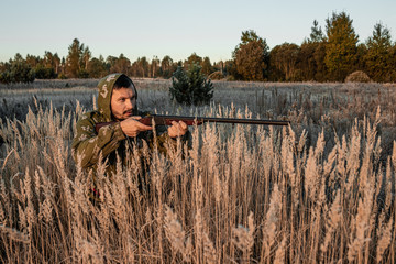 A hunter with a gun is sitting in the grass waiting for prey. The hunting period, the fall season is open, the search for prey.