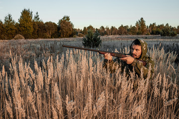 A hunter with a gun is sitting in the grass waiting for prey. The hunting period, the fall season is open, the search for prey.