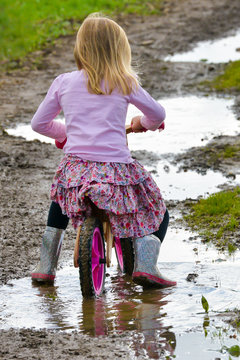 Rear view of young girl riding her bike through muddy  puddles