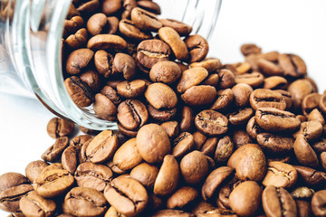 Roasted coffee beans rolling out of a glass jars isolated on white background.