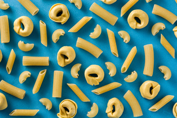 Different types of pasta pattern. Penne pasta and tortellini on blue background